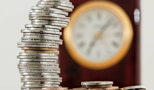 Zeit und Geld Münzen vor einer Wanduhr