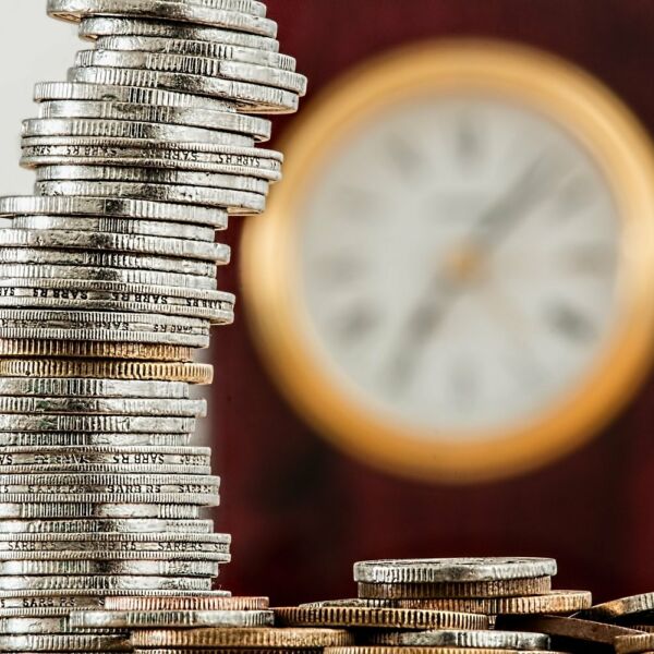 Zeit und Geld Münzen vor einer Wanduhr