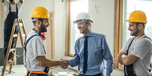 Handwerker und Auftraggeber geben sich die Hand bei einem Vor-Ort-Termin auf einer Baustelle