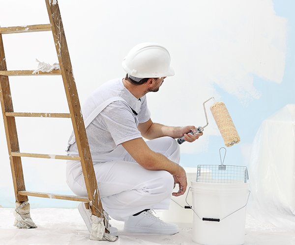 Maler streicht Wand mit Malerrolle in weißer Farbe.