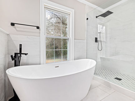 helles, freundliches Badezimmer mit großer Badewanne und Regendusche und schwarzen Armaturen