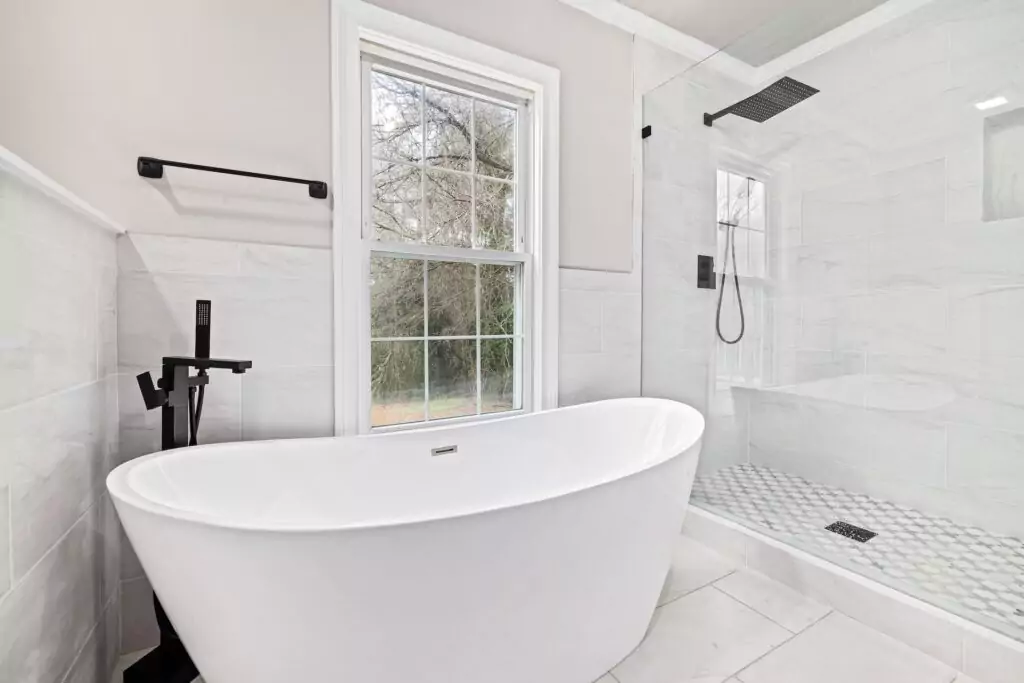 helles, freundliches Badezimmer mit großer Badewanne und Regendusche und schwarzen Armaturen