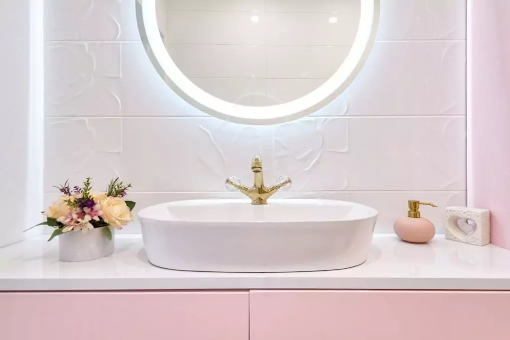 Waschtisch in einem hellen Bad in Weiß und Rosa mit beleuchtetem Spiegel
